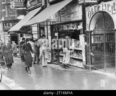 London im Frühjahr 1941 - Alltag in London, England Männer und Frauen halt in die Schlagzeilen zu sehen, wie Sie ein Kiosk auf dem Londoner Fleet Street vorbei. Das Old Bell Tavern ist auch auf der rechten Seite des Bildes sichtbar. Stockfoto