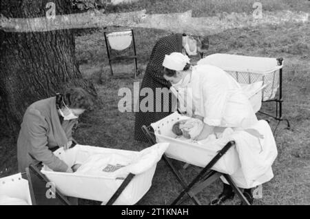 Herrenhaus wird Mutterschaft Startseite - Leben bei Brocket Hall, Welwyn, Hertfordshire, 1942 neue Mütter und eine Krankenschwester sammeln ihre Babys für die "Fütterung". Die Babys genießen ein open air Snooze. Die Frauen sind alle Tragen von Atemschutzmasken die Ausbreitung von Keimen zu verhindern. Stockfoto