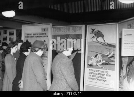 Ministerium für Information Ausstellungen während des Zweiten Weltkrieges, London, England, UK, 1943 eine Gruppe von Hausfrauen Blick auf eine Anzeige der russischen Plakate in einer Ausstellung, die wahrscheinlich in London statt. Die Ausstellung wird sowohl auf die Arbeit der Roten Armee haben und auch auf das normale Leben für Zivilisten in der Sowjetunion. Stockfoto