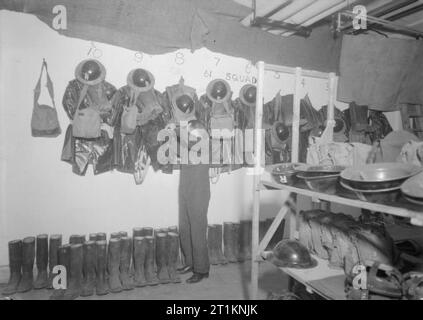 Air Raid Vorsichtsmaßnahmen bei Kingston House, Knightsbridge, London, England, C 1940 Mitglied der ARP-Personal prüft die anti-gas Kleidung und Ausrüstung von 61 Gruppe, die an der Wand am Kingston Haus hängt. Die Stahlhelme, Gasmasken, anti-gas Caps und Gummistiefel, die Linie der Wand wurden für den Einsatz bei einem Gasangriff unerlässlich. Beachten Sie auch die Zeilen der gespeicherten Ersatzteile Helme und Pflicht Gasmasken in Rucksäcke rechts im Vordergrund des Fotos. Der "R" auf seiner Tunika zeigt wahrscheinlich, dass er von einem rescue Party. Stockfoto