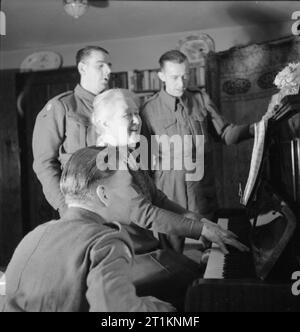 Frau Hornist geht in den Krieg - Alltag im East Dean, Sussex, England, 1943 Nach dem Tee, Frau Hornist sitzt am Klavier, führt Ihr Soldat Gäste (einschließlich Harry Wardle (stehend links) und Harry Baddeley (stehend rechts)) singend. Stockfoto