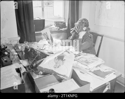 Air Raid Vorsichtsmaßnahmen in Großbritannien - das Personal des Ministeriums für Informationen tragen Gasmasken zu arbeiten, London, England, 1941 Miss Marjorie Lloyd des Nahen Ostens Abteilung des Ministeriums für Informationen sitzt an ihrem Schreibtisch das Tragen eines zivilen Gasmaske. Ihr Job ist, Fotos in London für den Versand zu "Parade"-Magazin zu wählen. Stockfoto