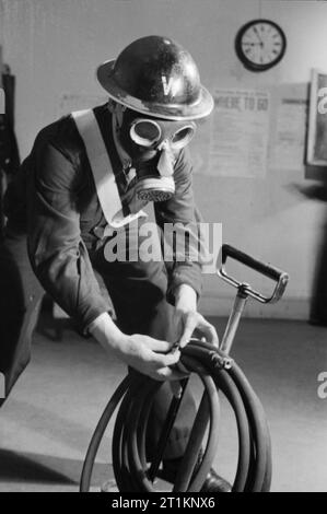 Air Raid Vorsichtsmaßnahmen auf der British Home vorne, C 1941 einem Luftangriff Warden Tragen seiner Stahlhelm und Pflicht Gasmaske prüft, ob seine Kübelspritze, um auf seinem Posten, irgendwo in Großbritannien, c 1941. Stockfoto