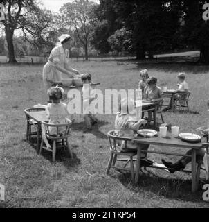 Kindergarten - Leben im alten Herrenhaus, Wendover, Buckinghamshire, England, 1944 eine Krankenschwester serviert Mittagessen für Kinder, die an Tischen und Stühlen sitzen, die auf dem Gras in den sonnigen Garten der Kindergarten im alten Herrenhaus in Wendover. Die Legende besagt, dass, wo immer möglich, mit den Kindern die Mahlzeiten werden im Freien serviert. Stockfoto