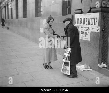 Nacht School Girl - Abendkurse in Kriegszeiten London, C 1940 Frau Ridley hält eine Zeitung von einem Straßenhändler kaufen. An der Wand ein Zeichen für einen Luftschutzbunker deutlich zu sehen ist. Stockfoto