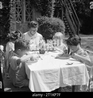 Kindergarten - Leben im alten Herrenhaus, Wendover, Buckinghamshire, England, 1944 eine Krankenschwester setzt sich mit einigen der älteren Kinder an einem Tisch im sonnigen Garten des Kindergarten im alten Herrenhaus in Wendover zu essen. Die Legende besagt, dass, wo immer möglich, mit den Kindern die Mahlzeiten werden im Freien serviert. Eine kleine Vase mit Blumen schmückt den Tisch. Im Hintergrund, die kreuz und quer von Tape auf die Fenster der Schule, blast, um Schäden zu verhindern, können gerade gesehen werden. Stockfoto