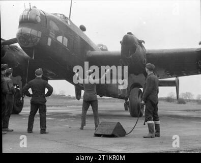 Royal Air Force Bomber Command, 1942-1945. Der Unteroffizier verantwortlich für eine Wartung Mannschaft leitet ein Handley-Page Halifax Mark II von Nr. 1656 Schwere Umstellung Einheit auf die Streuung an Lindholme, Yorkshire, während andere Besatzungsmitglieder sind bereit, mit Keil - Bausteine. Stockfoto