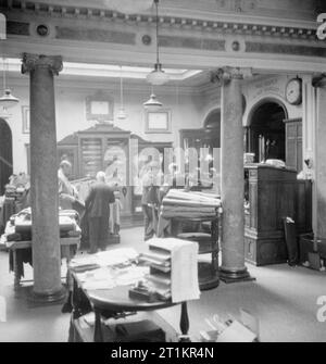 Savile Row - Tailoring bei Henry Poole und Co., London, England, UK, 1944 Kunden untersuchen die Backwaren der Henry Poole und Co. in das 18. Jahrhundert Showroom in der Savile Row. Im Hintergrund zu sehen ist ein großer Schrank, in dem werden verschiedene Schwerter und verschiedene militärische Kleid Uniformen angezeigt. Die Ursprüngliche Bildunterschrift erklärt, dass, obwohl die Palette der verfügbaren Materialien, sehr begrenzt ist, "einige der Vorkriegszeit stopft noch auf Lager und der britische Hersteller weiterhin eine begrenzte Menge feinen worsteds und tweeds" drehen. Stockfoto