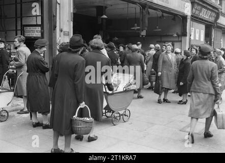 Käufer Warteschlange für Gemüse außerhalb der Gemüsehändler Shop, 'J Holz", 97-99 High Road, Wood Green, London 1945. Massen von Frauen, die das Pflaster, wie sie für Gemüse außerhalb der Gemüsehändler shop Queue, 'J Holz", 97-99 High Road, Holz Grün. Viele haben Babys im Kinderwagen. Gerade sichtbar rechts auf dem Foto ist der Shop 'Jolly', die verkauft" zubereitet Bestimmungen fertig auf dem Tisch, wie zum Beispiel Torten, Gebäck und Sandwiches. Stockfoto