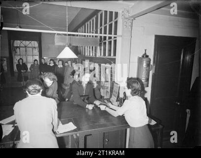 16-jährigen Registrieren - Jugendliche ihre Erwachsenen ID-Karten von der Labour Exchange, London, England, UK, 1945 der 16-jährige Patricia D Harding (Mitte rechts), eine Schreibkraft Telefonistin für ein Bauunternehmer, erhält Ihre neue Blau (Erwachsene) Personalausweis von einem Ministerium für Arbeit Beamter im Arbeitsamt, Islington. Gemäß der ursprünglichen Caption, geht sie zu Abend Klassen und ist Mitglied des London Girls' Club der "Kopenhagener Freizeit Club" genannt. Viele andere Mädchen können im Hintergrund gesehen werden, die wiederum das Warten an den Schreibtisch. Verschiedene Plakate sind auch sichtbar im Raum. Stockfoto