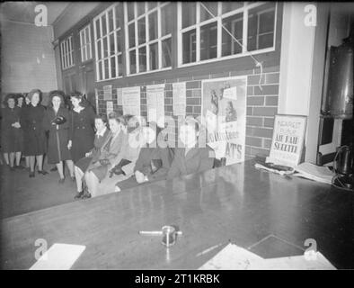 16-jährigen Registrieren - Jugendliche ihre Erwachsenen ID-Karten von der Labour Exchange, London, England, UK, 1945 Mädchen im Teenageralter ihren biegen Sie am Schreibtisch am Arbeitsamt, Islington erwarten. Sie stehen Schlange für Ihre neuen Erwachsenen Identität Karten zu registrieren. Hinter ihnen, verschiedene Einstellung Poster gesehen werden kann. Stockfoto