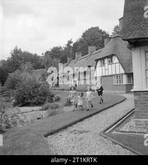 Die Cottages von Freefolk - Leben im Dorf Freefolk, Hampshire, England, Großbritannien, 1943 eine Gruppe von Kindern beim Spielen auf dem Rasen neben der Blumenbeete außerhalb der Reihe von Hütten in Freefolk, Hampshire. Die Häuser sind weit zurück von der Straße und die kieswege und große Gärten alle Kinder in Sicherheit zu spielen, abseits vom Verkehr. Stockfoto