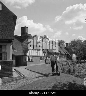 Die Cottages von Freefolk - Leben im Dorf Freefolk, Hampshire, England, Großbritannien, 1943 Ein Einwohner des Dorfes Freefolk den Rasen mäht im Sonnenschein. Von Interesse sind die Regen Wasserrinnen, das sich auf dem Boden entlang laufen direkt unterhalb der Kanten des Daches. Installiert, anstatt Dachrinnen, sie waren nötig, als "eavestroughs kann nicht angebracht zu Thatch' werden. Stockfoto