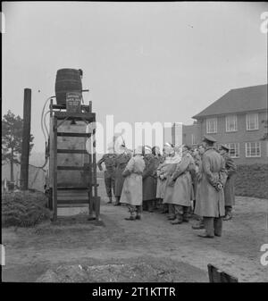 US-Truppen an der Britischen Armee Schule - amerikanische Soldaten trainieren in der Britischen Armee Schule der Hygiene, UK, 1944 als Teil der Kurs, den sie in der britischen Armee Schule der Hygiene, eine Gruppe von britischen Offizieren sind sehen Sie eine Demonstration der "improvisierte Dusche Badewanne für den Einsatz im Feld. Die Dusche besteht aus einem großen Fass auf einem Holzrahmen. Verschiedenen Riemenscheiben kontrollieren den Fluss von Wasser aus dem großen Fass auf ein kleineres Fass komplett mit Duschkopf. Stockfoto