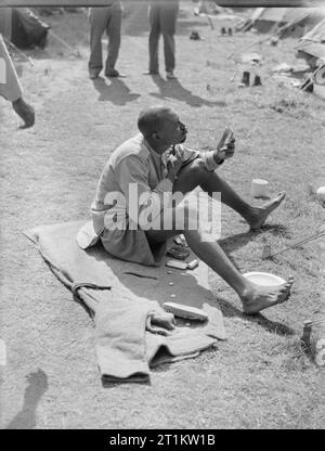 Sieg Marchers Camp in London - Unterkünfte in Kensington Gardens, London, England, UK, 1946, einer Westafrikanischen Soldaten rasiert in der Vorbereitung für die Siegesparade in London. Er sitzt auf einer Decke auf der Wiese neben dem Tented Camp, in dem er und viele andere Soldaten, Wohnen, in Kensington Gardens. Stockfoto