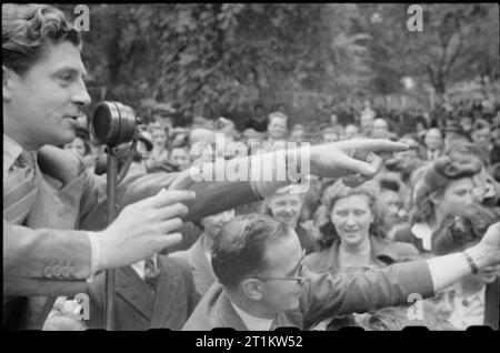 War Fair- Holidays at Home at a Fete am Russell Square, London, 1943 Film- und Bühnenschauspieler Derek de Marnay steht an einem Mikrofon und zeigt auf jemanden in der Menge, während er eine sehr kleine, sehr grüne Banane im Rahmen der Feierlichkeiten am Russell Square versteigert. Nach der Originalüberschrift wurde das Stück Frucht "GBP 5" geholt. Stockfoto