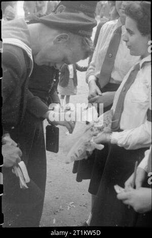 Krieg Fair - Urlaub zu Hause auf einer Fete in Russell Square, London, 1943 Ein holländischer Seemann hält ein raffle Tickets von einem Mitglied des Roten Kreuzes Kadetten am Russell Square fete kaufen. Der Preis ist ein Modell Schlachtschiff. Stockfoto