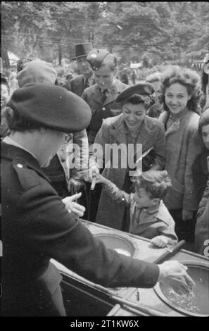 Krieg Fair - Urlaub zu Hause auf einer Fete in Russell Square, London, 1943 ein Junge, von seiner Mutter geholfen hat, genießt ein Spiel von magnetischen Angeln auf ein von einem Mitglied des Roten Kreuzes am Russell Square fete ausführen. Zivilisten und ein Mitglied der Royal Air Force auf. Stockfoto