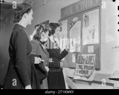 Das Wohlbefinden der Beschäftigten zu einem Royal Ordnance Factory - Leben in Rof Bridgend, Januar 1942 Frauen Krieg Arbeitnehmer bei ROF Bridgend Blick am Schwarzen Brett von sozialen Aktivitäten im Werk zur Verfügung. Eine Frau weist auf ein Plakat mit der Aufschrift "Geschwindigkeit auf YWCA'. Das Programm für die Aktivitäten der Woche ist 5-11. Januar 1942 datiert. Ein anderes Plakat wirbt für "goldene Handschuhe' und 'Mädchen von der Avenue 1', die in Pencoed Kino gezeigt wird. Stockfoto