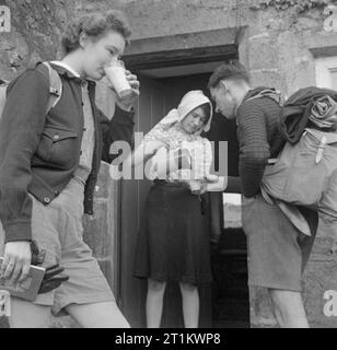 Junge Wanderer in Yorkshire - die Arbeit der Youth Hostel Association in Wartime, Malham, Yorkshire, England, Vereinigtes Königreich, 1944 Wanderer Joan (links) und Sydney (rechts) Sidwell aus Barking in Essex halten an einem Bauernhaus in den Yorkshire Dales für ein Glas Milch. Die Sidwells machen einen Wanderurlaub in den Pennines und wohnen im Youth Hostel in Malham. Stockfoto