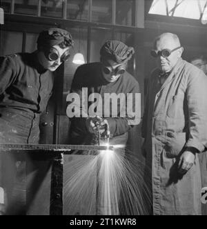 Zaunkönige Zug für neuen Job-Training für Schiffsmechaniker der Royal Naval der Frauen Service, England, UK, 1943 die Funken fliegen, als Mitglied des WRNS schneidet eine Eisenstange über einen Gasschweißbrenner als Teil ihrer Ausbildung als Schiffsmechaniker (LC), vermutlich an der Slough Regierung Training Center. Sie ist von Ihrem Instruktor und anderen Zaunkönig beobachtet. Alle tragen Sie eine Schutzbrille. Stockfoto