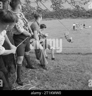 Jugendversammlungen - Ausbildung Für Jugendorganisationen, Sidcot School, Winscombe, Somerset, England, Großbritannien, 1943 Pfadfinder halten sich fest an den Seilen, während ein Girl Guide auf einer Seilbrücke gleitet, die sie alle gerade gebaut haben. Die Brücke wurde im Rahmen eines Campings und Holzhandwerks im Rahmen des einwöchigen Jugendtrainings an der Sidcot School in Somerset gebaut. Stockfoto