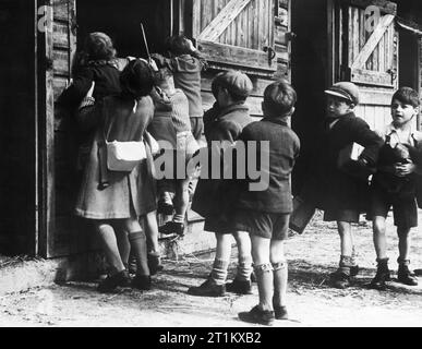 Eine Gruppe der evakuierten Besuch eines Bauernhofes bei einem Spaziergang durch die Natur von ihrer Billet in Dartington Hall in Totnes, Devon während 1941. Eine Gruppe junger Umsiedler schauen Sie über eine stabile Tür, um zu sehen, wenn sie das Pferd, das Innere sehen kann. Alle Kinder sind mit ihren Gasmasken in Kartons. Sie haben auf diesem Bauernhof als Teil ihrer Natur zu Fuß von ihren Billet gestoppt in Dartington Hall in Totnes, Devon, wo 250 Umsiedler aus London und Gravesend in Kent wohnen. Stockfoto