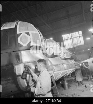 Geburt eines Bombers - Flugzeugbau in Großbritannien, 1942 Lackierer bei der Arbeit in der Lackiererei der Handley Page Factory beim Cricklewood. Papier wurde über die Fenster der vorderen Revolver, Cockpit und Bombe aimer Fahrgastraum dieser Halifax geklebt, um das Glas von der Lackierung zu schützen. Stockfoto