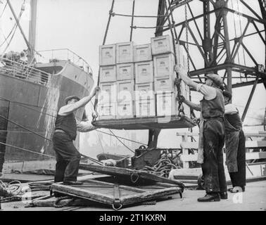 Großbritannien liefert die Ware in Kriegszeiten - Hafenarbeiter in Bristol, England, 1940 Fälle von Gut durch Kran auf einen warten Dampfgarer zu einem Bristol Dock geladen werden. Jeder der Kisten ist mit einem Union Jack und die Worte "Großbritannien liefert die Ware" gestempelt. Stockfoto