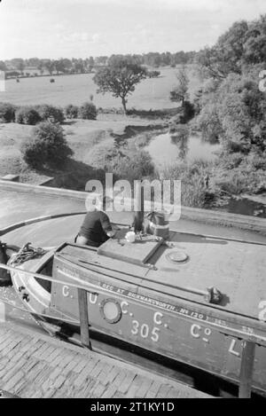 Britische Kanäle in Kriegszeiten - Verkehr in Großbritannien, 1944 ein Kanal Boot registriert in Rickmansworth (wahrscheinlich vom Gribbis Familie) Reisen in die Sonne über dem Aquädukt, die die Grand Union Canal führt über den Fluss Nene in der Nähe von Wolverton, Buckinghamshire. Der Bootsmann, wahrscheinlich Herr Gribbis, Lenkung das Boot auf dem aquädukt gesehen werden kann, und bewundern Sie die Aussicht auf die Landschaft. Ihm unten, einen Mann gesehen werden kann genießen beim Angeln am Fluss Nene. Stockfoto