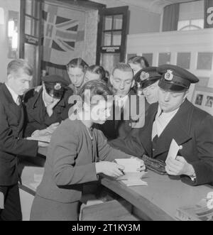 Ein Matrose der Handelsmarine zur Stadt kommt - die Arbeit der Handelsmarine Club, Piccadilly, London, 1942 25 Jahre alte Seeleute Richard Pates im Merchant Marine Club in Piccadilly kommt an und wird durch die weibliche 'Guide' begrüßt, Frau Elsie Clunas in der Eingangshalle. Elsie ist von allen an der Verein bekannt als "Tante Elsie", trotz der Tatsache, dass sie nur 27 Jahre alt ist. Sie ist auch als "Geordie" Clunas bekannt, denn sie ist von Newcastle. Vor dem Krieg war sie ein schaufensterdekorateur. Mehrere andere Seeleute warten auf Ihre biegen Sie an der Theke, während andere sich von einem männlichen Club 'Guide' geholfen. Stockfoto