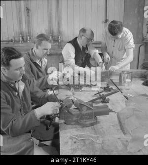 Britische bieten Kunsthandwerk für Amerikanische Rekonvaleszenten - Erholung für verwundete Soldaten auf 159 US General Hospital, Yeovil, Somerset, England, UK, 1945 Pfeife rauchende Reg Hawkins (Meister des Holzes Mühle an der Westlands Pflanze, zweiter von rechts) hilft PBP R Covey (rechts), um eine beschädigte Windschutzscheibe aus Plexiglas im Handwerk workshop Schnitt bei 159 US General Hospital, Yeovil. PSC K Elternteil (links) und T/S WA McKinney (zweiter von links) Teile dieser zurückgefordert Plexiglas zu machen ein Armband (Eltern) und ein Foto rahmen (McKinney). Stockfoto