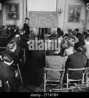 Briten lernen Türkisch - Erwachsenenbildung in London, 1943 Bay (Mister) Ali R?za?encan, Sekretär der Halkevi, zeigt auf die Tafel, während er die Klasse über die drei verschiedenen Pronomen-Suffixe unterrichtet. Die Studenten sitzen in Reihen in einem reich verzierten Raum, an den Wänden sind Porträts von König Georg VI. Und Präsident Inonu zu sehen. Türkisch Sprachkurse finden hier zweimal pro Woche statt.Türkisch: ?Ngilizler Türkce Ö?reniyor - Londra'da Yeti?kin E?itimi, 1943Halkevi Sekreteri Bay Ali R?za?encan, s?n?fa üc farkl? ki?i zamiri ekini ö?retirken tahtay? ich bin Ediyor. S?n?f?n?n ön s?ras? onu dikkatle di Stockfoto