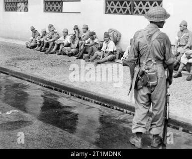 Britische Wiederbesetzung von Singapur, 1945 ein Soldat aus der 5. indischen Division wacht über japanischen Gefangenen außerhalb ihrer ehemaligen Hauptsitz in Singapur. Stockfoto