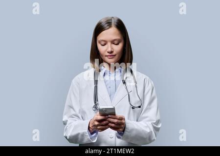 Junge Ärztin, Medizinstudentin mit Smartphone auf grauem Hintergrund Stockfoto