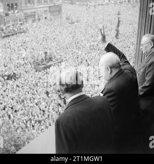 Winston Churchill winkt in Whitehall in London zu Menschenmengen, während sie den VE Day, den 8. Mai 1945, feiern. Vom Balkon des Gesundheitsministeriums aus gibt Premierminister Winston Churchill am 8. Mai 1945 (VE Day) sein berühmtes „V for Victory“-Zeichen an den Tag in Whitehall, an dem er der Nation den Sieg des Krieges mit Deutschland mitbrachte. Zu Churchills Linken steht Sir John Anderson, der Schatzkanzler. Zu Churchills Recht steht Ernest Bevin, der Arbeitsminister. Stockfoto