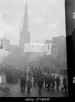 Operation Moonlight Sonata - Bombenschaden in Coventry, November 1940 Truppen marschieren am 16. November 1940 durch das Zentrum des verwüsteten Coventry. Im Hintergrund befinden sich der Turm und der Turm der Pfarrkirche der Heiligen Dreifaltigkeit. Ein Großteil der Stadt wurde bei einem schweren deutschen Luftangriff in der Nacht vom 14. Auf den 15. November 1940 zerstört. Stockfoto