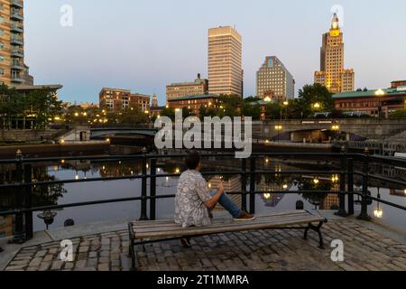 Ein einsamer Mann sitzt auf einer Parkbank am Riverwalk in Downtown Providence Stockfoto