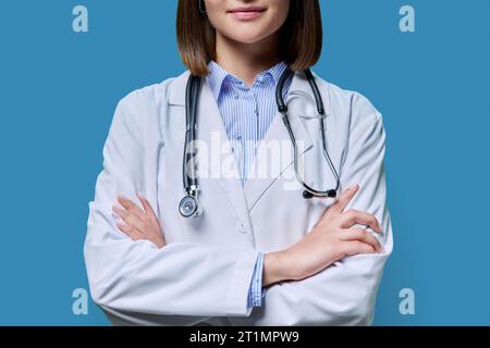Nahaufnahme der selbstbewussten Haltung einer Ärztin mit überkreuzten Armen auf blauem Hintergrund Stockfoto