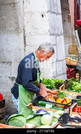 Ein lokaler französischer Stallhalter bereitet seine Produkte an einem Gemüsestand auf dem lokalen Lebensmittelmarkt in der Altstadt von Annecy, Frankreich, zu Stockfoto