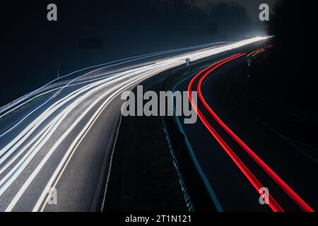 Abstraktes Bild von Nachtverkehrsampeln auf der Straße. Autolichtwanderungen bei Nacht auf kurvigen Asphaltstraßen. Langzeitbelichtung mit Fahrzeugbewegungen Stockfoto
