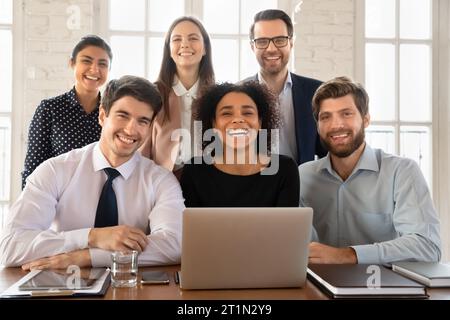Fröhliches, junges multiethnisches Team posiert am Arbeitstisch Stockfoto