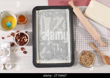 Ich mache köstliche Baklava. Backpfanne mit Teig und Zutaten auf weißem Holztisch, flach liegend Stockfoto