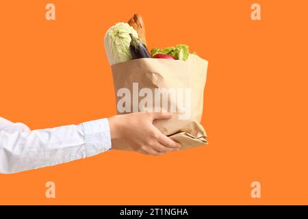 Frau, die Papiertüte mit frischem Essen auf orangem Hintergrund hält Stockfoto