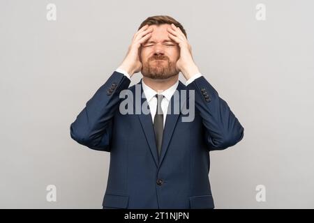 Geschäftsmann berührt Kopf mit runzelndem enttäuschtem krankhaftes emotionales Gesicht isolierter Studio-Hintergrund. Stockfoto