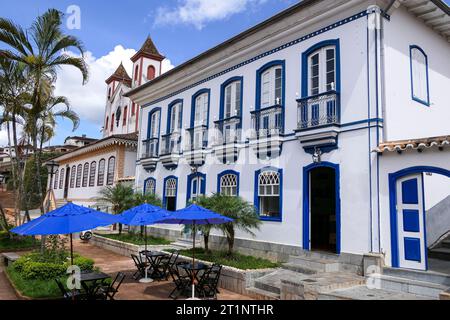 Blick auf das wunderschöne historische Gebäude und die Kirche, mit Palmen und blauem Himmel mit weißen Wolken, Serro, Minas Gerais, Brasilien Stockfoto