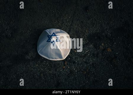 Gestrickte Kippahmütze im Stil der israelischen Flagge auf dunklem Asphaltgrund Stockfoto