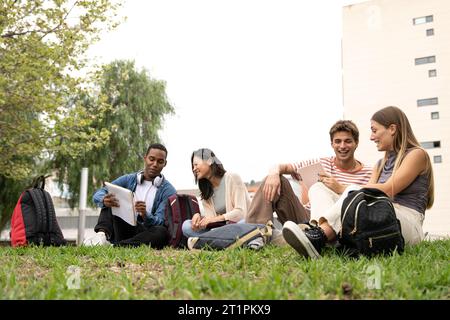 Verschiedene Gruppen von Studenten, die draußen sitzen und Dokumente lesen. Glückliche multirassische Leute, die auf dem Boden Campus sitzen. Stockfoto