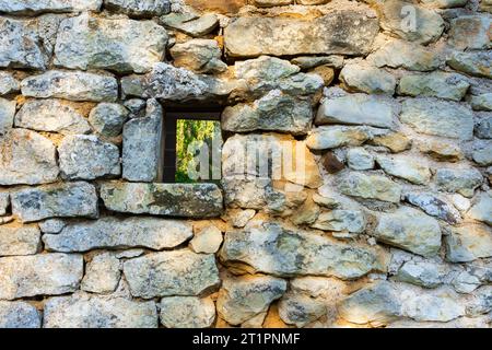 Zufällige Steinmauer mit kleinen quadratischen Fenstern im Bauernhaus - Zentralfrankreich. Stockfoto