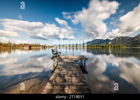 Wolken, die über eine hölzerne Fußgängerbrücke am Ufer des Kochelsees vor herbstlicher Berglandschaft treiben und Wolken am Himmel, Bayern Stockfoto